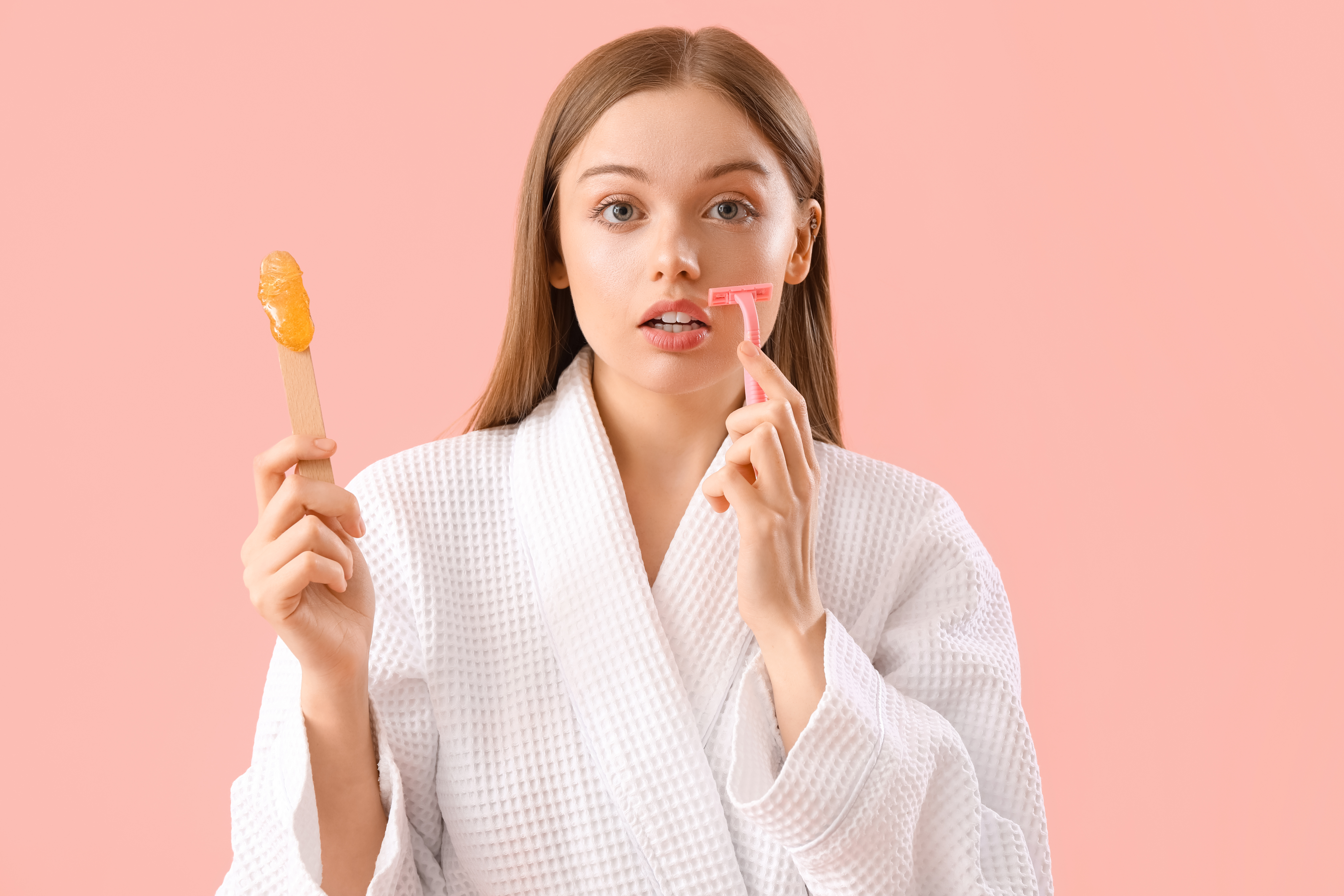 Young woman holding spatula with sugaring paste and razor on pin Dame mit Rasierer und Heißwachs in der Hand