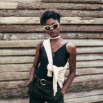 nsey-benajah-eqhkEKsurbo-unsplash Dame mit Sonnenbrille vor einem Holzstoß
